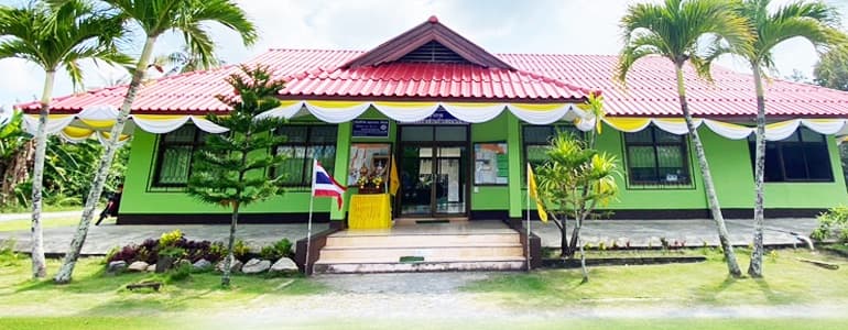 อาคารที่ทำการองค์การบริหารส่วนตำบลขนาบนาก หลังคาสีแดง ผนังสีเขียว ประดับผ้าระบายเหลืองขาว มีต้นหมากเรียงหน้าอาคาร